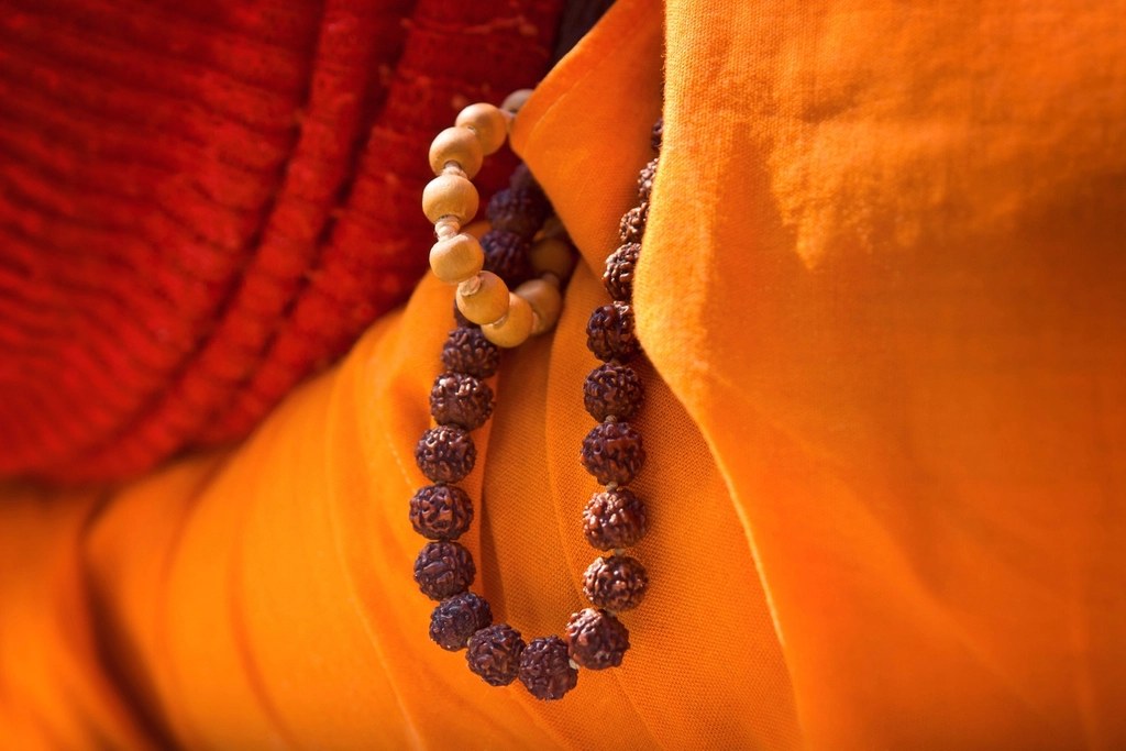 Mãos segurando um japamala de sementes de rudraksha sobre roupa laranja
